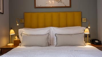 A hotel room with a large bed, two bedside lamps, a framed artwork above the bed, and a wooden headboard.