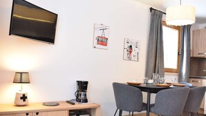 Eine moderne Küche mit Flachbildfernseher, Kaffeemaschine und einem Essbereich mit Tisch und Stühlen.