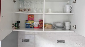 Une cuisine avec des meubles blancs, une étagère où sont rangés des verres et divers produits alimentaires.