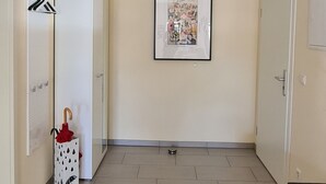 Un couloir avec une armoire blanche, un tableau encadré au mur et un petit panier blanc contenant un parapluie rouge.