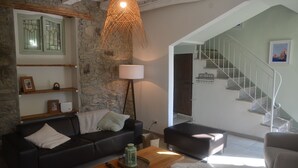 A living room with a stone wall, a black leather sofa, a wooden coffee table, a floor lamp, and a staircase leading to an upper floor.