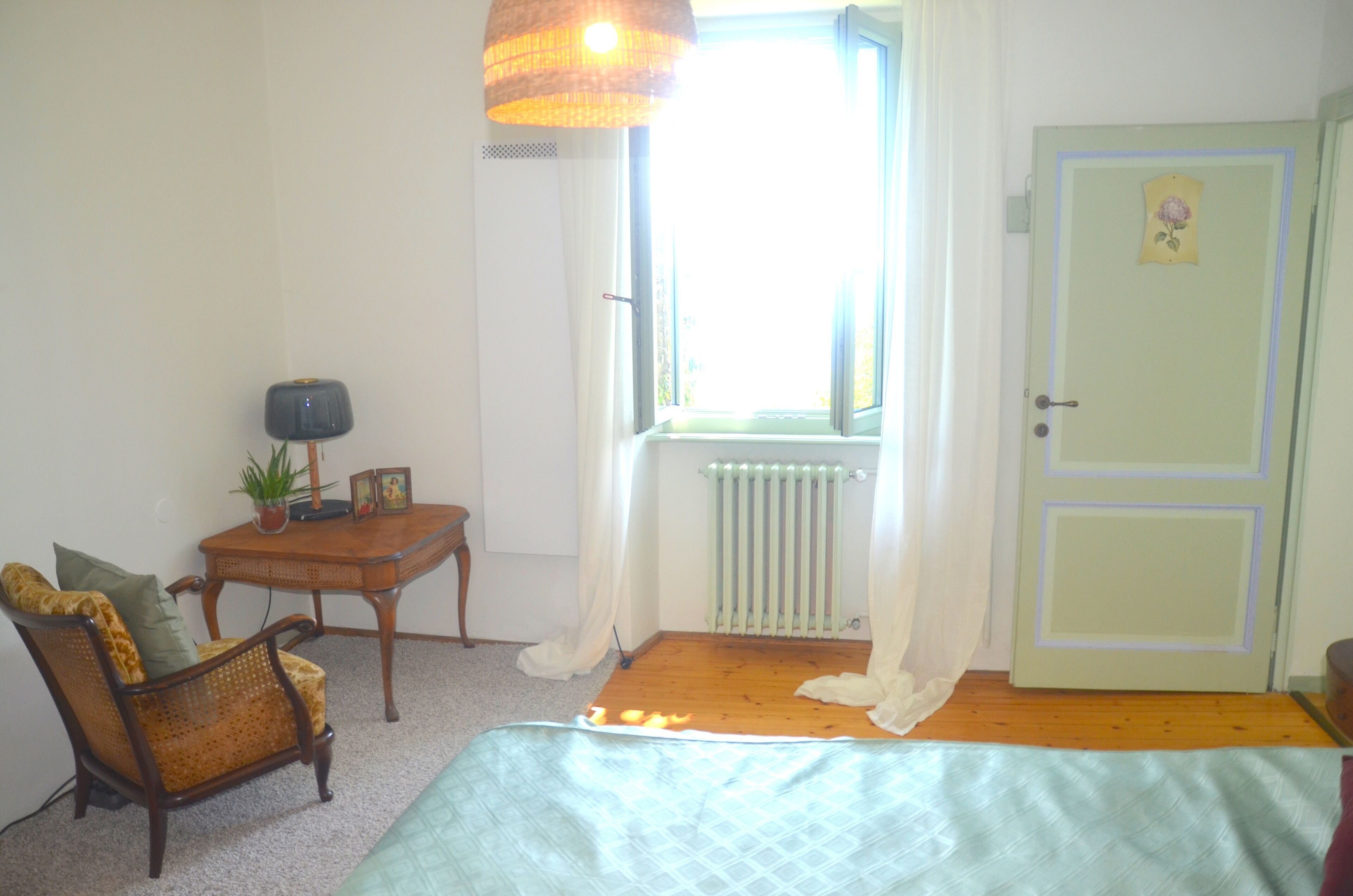 Una habitación con una cama, una silla, una mesita de noche con una lámpara, un radiador y una puerta decorada con flores.