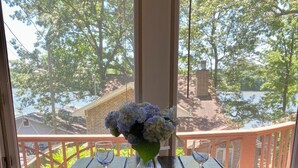 Une table en bois, ornée d’un vase de fleurs et de verres à vin, sur un balcon donnant sur un lac.