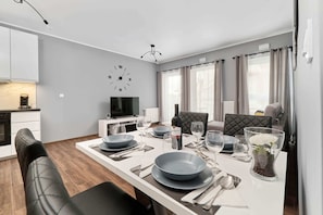 A modern dining area with a white table set for four, a television, and a clock on the wall. - Spacious Apartment in Wroclaw | Parking | 2 Balconies (Wroclaw)