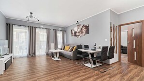 Ein modernes Wohnzimmer mit einer Couch, einem Esstisch, Stühlen, einem Fernseher und einem großen Fenster mit Vorhängen.