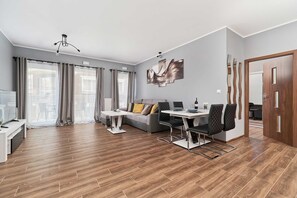Una sala moderna con sofá, mesa de comedor, sillas, televisor y un amplio ventanal con cortinas.