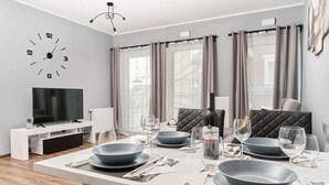Ein moderner Essbereich mit Esstisch, gedeckt für vier Personen, einem Flachbildfernseher und einem großen Fenster mit Vorhängen.