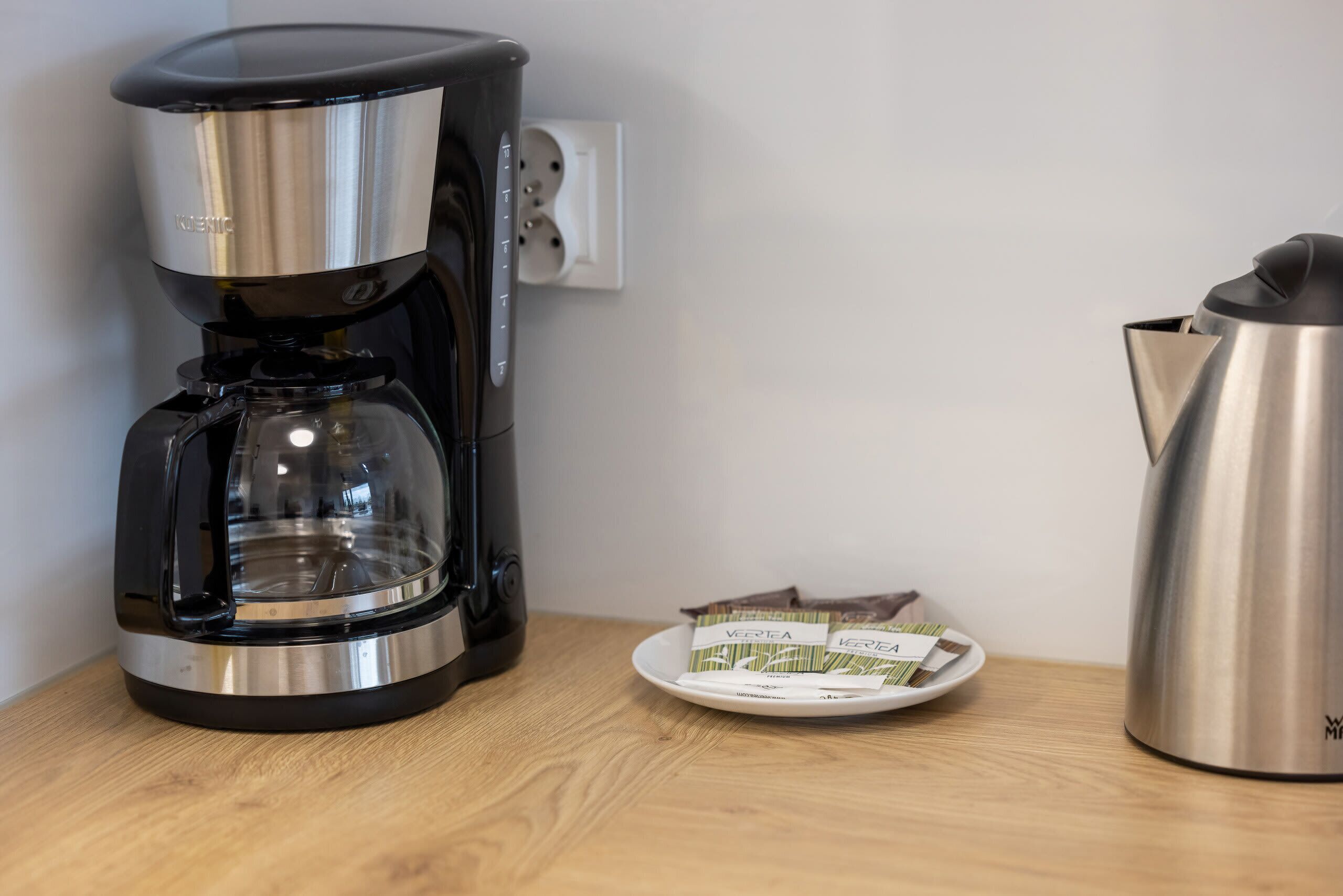A coffee maker, a plate with coffee pods, and a kettle on a wooden surface.