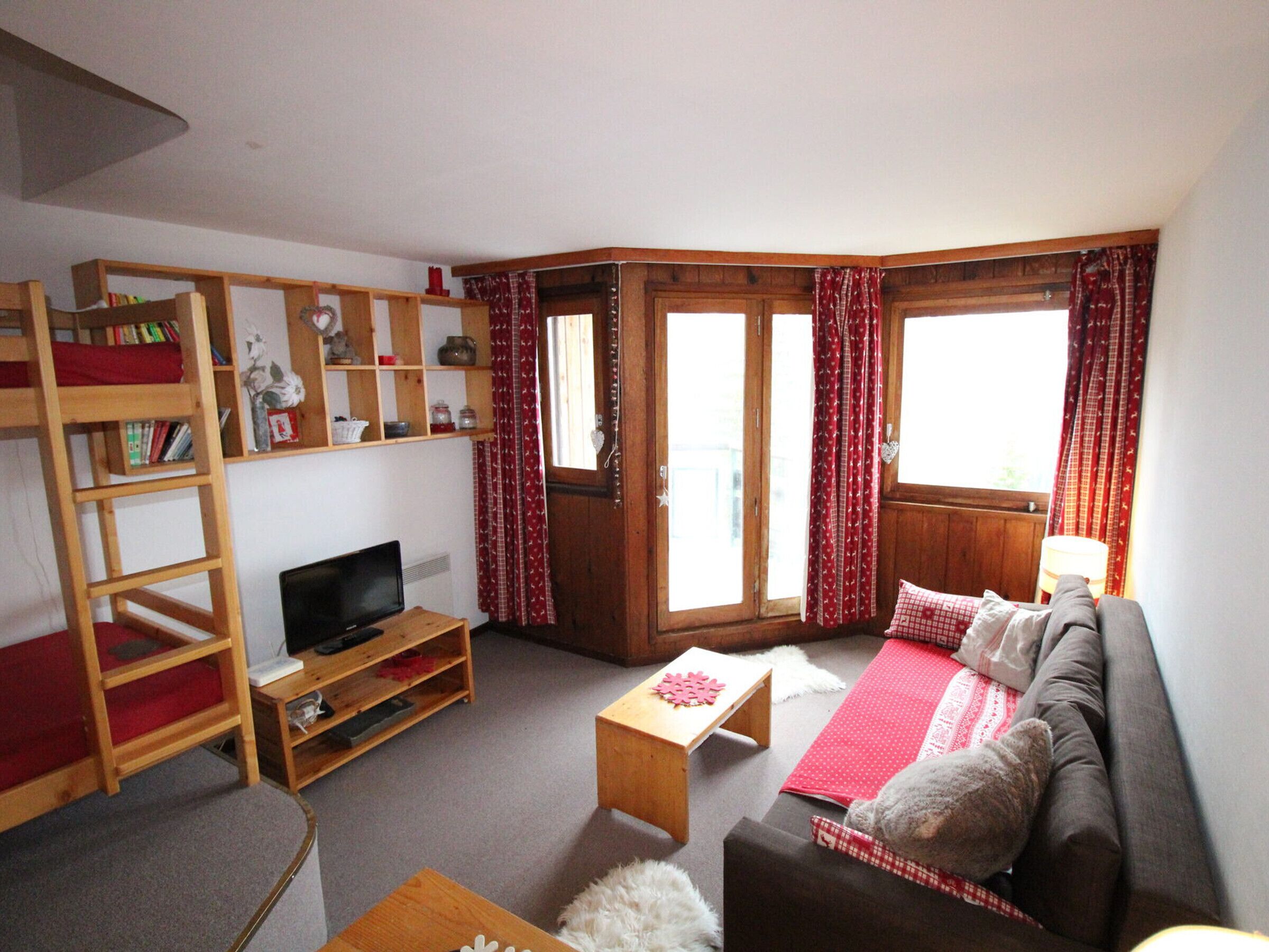 A cozy living room with a sofa, a TV, a wooden bookshelf, and a window with curtains.