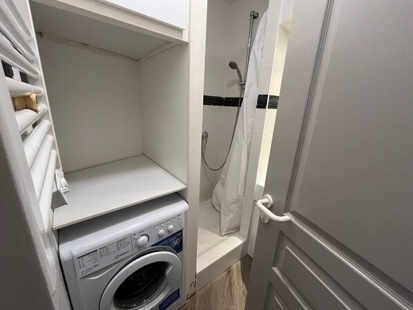 A compact laundry room with a front-loading washing machine and a shower area.