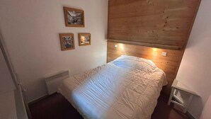 Quarto com cabeceira de madeira, cama com edredom branco e três quadros na parede.