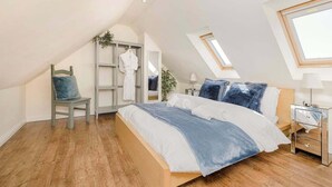 Un dormitorio con techo inclinado, una cama con ropa de cama azul, una silla, un armario y una mesita de noche.