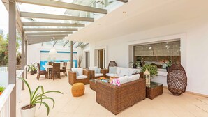 A spacious patio with wicker furniture, a glass ceiling, and potted plants.