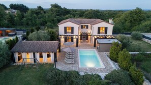 Una casa de dos pisos con piscina, mobiliario de exterior y una pérgola.