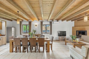 Un salón amplio con techo de madera, una mesa de comedor preparada para cuatro personas, un sofá y un televisor.