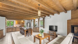 Un amplio salón con techo de madera, un conjunto de sofás, una mesa de comedor con sillas, una zona de cocina y un televisor.