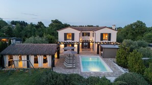 Una casa de dos pisos con piscina, mobiliario exterior y un porche cubierto.