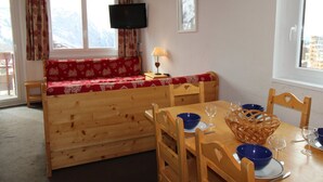 Tunnelmallinen huone, jossa on puinen penkki, ruokapöytä tuoleineen, seinälle asennettu televisio ja ikkuna, jossa on verhot.