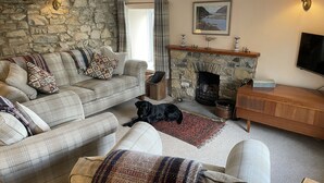 A cozy living room with a stone wall, a fireplace, a sofa set, and a television. - Penllain (Newport)