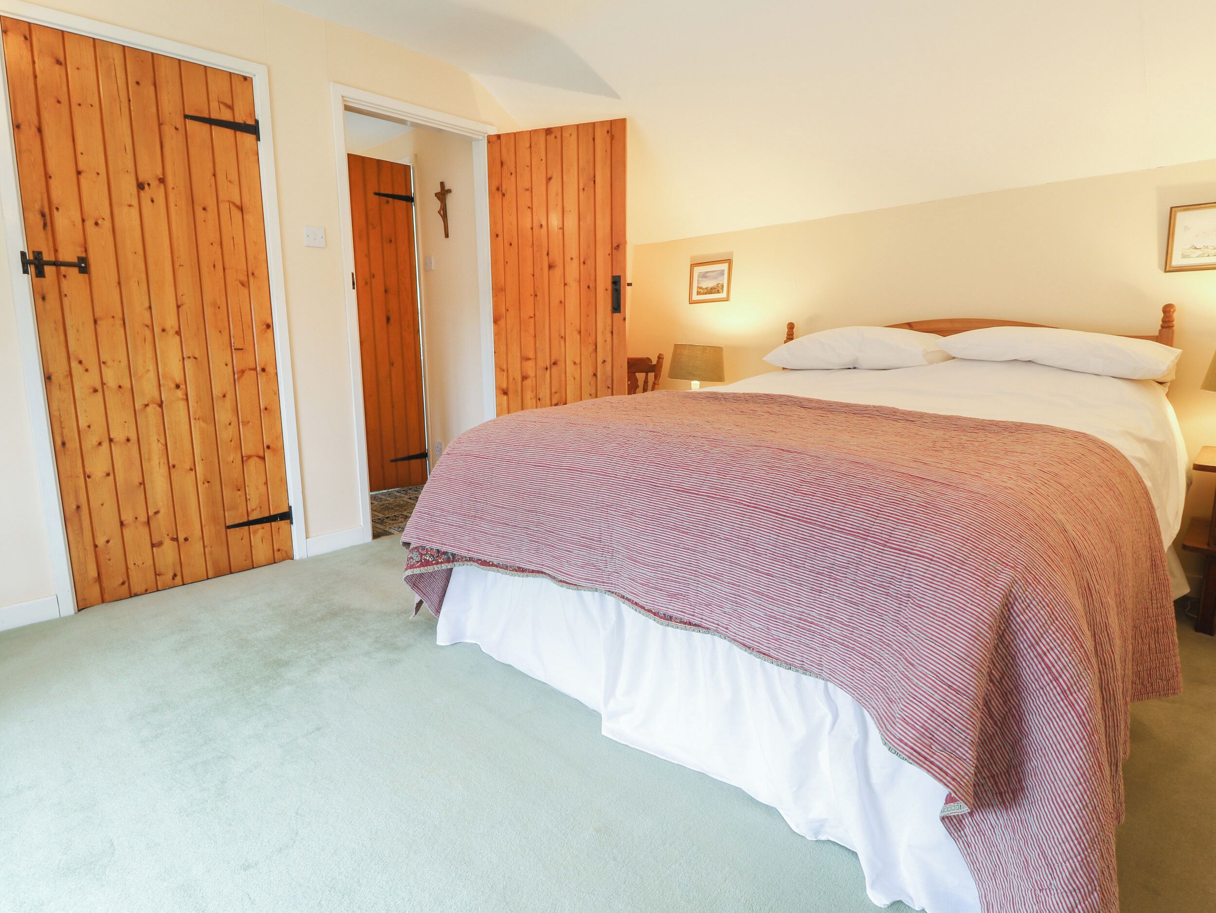 A bedroom with a bed, a wooden door, a cross on the wall, and a framed picture.