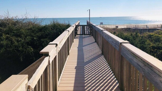 A wooden boardwalk leading to a beach with a clear view of the ocean.