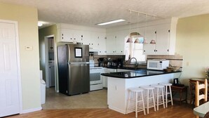 A kitchen with a central island, white bar stools, a refrigerator, a microwave, and a sink.