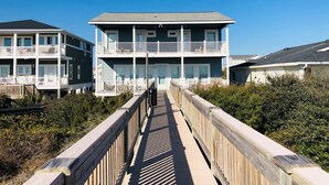 A beachfront property with a wooden boardwalk leading to a two-story building with balconies.