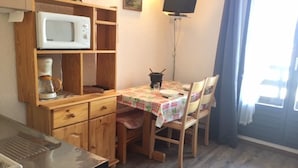 Kompakti keittiö, jossa on mikroaaltouuni, kahvinkeitin ja pieni ruokapöytä tuoleineen.