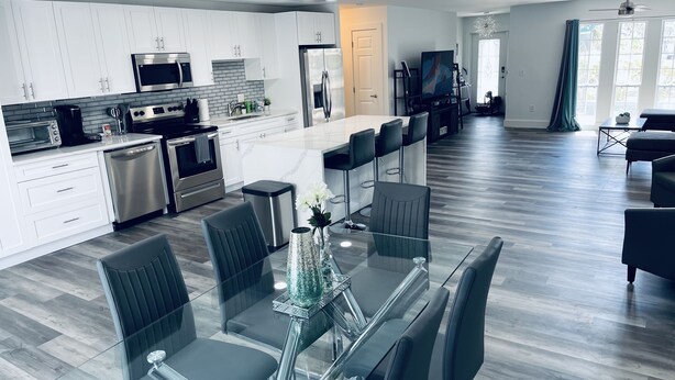 A modern kitchen with white cabinets, stainless steel appliances, and a dining area with a glass table and black chairs.