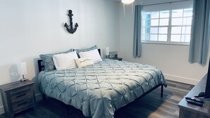 A neatly arranged bedroom with a bed, bedside tables, a nightstand, a ceiling fan, and a window with curtains.