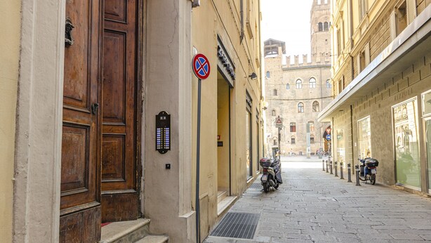Una calle estrecha con una puerta de madera, un cartel de 'prohibido estacionar' y una motocicleta estacionada al lado.