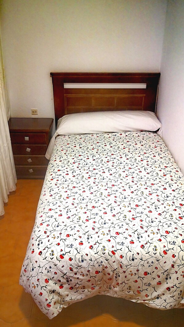 Una cama individual con una colcha estampada de flores, un cabecero de madera y una mesita de noche con cajones.