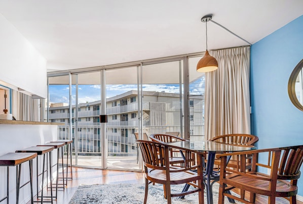 Ein modernes Zimmer mit einer großen Schiebeglasdoor zum Balkon, Holzmöbeln und Blick auf ein Gebäudekomplex.