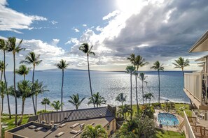 A rooftop pool area with lounge chairs, palm trees, and a view of the ocean.