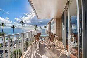 Ein Balkon mit Tisch und Stühlen, der Blick auf einen Strand mit Palmen und den Ozean bietet.