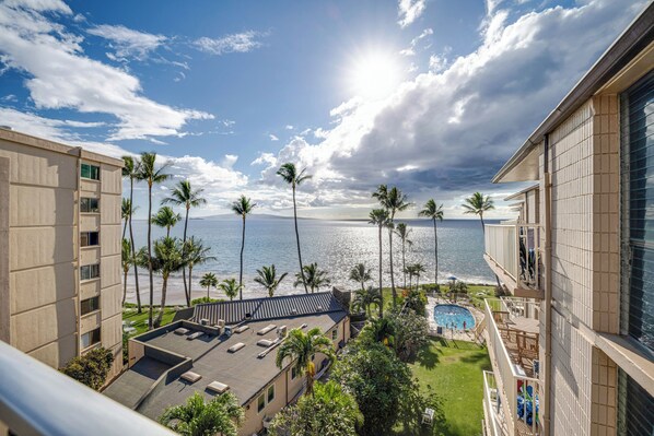 A hotel with a rooftop pool, palm trees, and a view of the ocean.