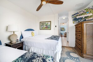 Une chambre d’hôtel avec deux lits, un ventilateur de plafond, une commode en bois et un grand tableau encadré au mur.