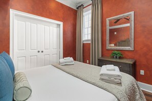 Una habitación de hotel con una cama grande, una puerta blanca, un espejo y una ventana con cortinas.