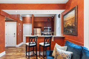 A modern kitchen with a bar area, two bar stools, and a dining table.