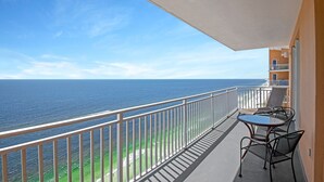 A balcony with a view of the ocean, a table, and two chairs.