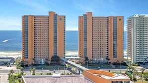 A high-rise hotel with multiple floors, a beach view, and a pedestrian bridge connecting to the beach.
