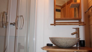 Un bagno con doccia in vetro, un mobile bagno in legno con lavabo a incasso, uno specchio e un porta asciugamani.