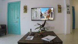 A living room with a teal door, a mounted TV displaying a street scene, a wooden table with a plant, and a sofa. - Casa Mixa con Decoración Exclusiva, Estilo Industrial (Mijas)
