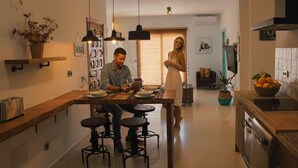 A modern kitchen with a wooden countertop, bar stools, and pendant lighting. There is a dining table with chairs, a basket of flowers, and a potted plant. - Casa Mixa con Decoración Exclusiva, Estilo Industrial (Mijas)
