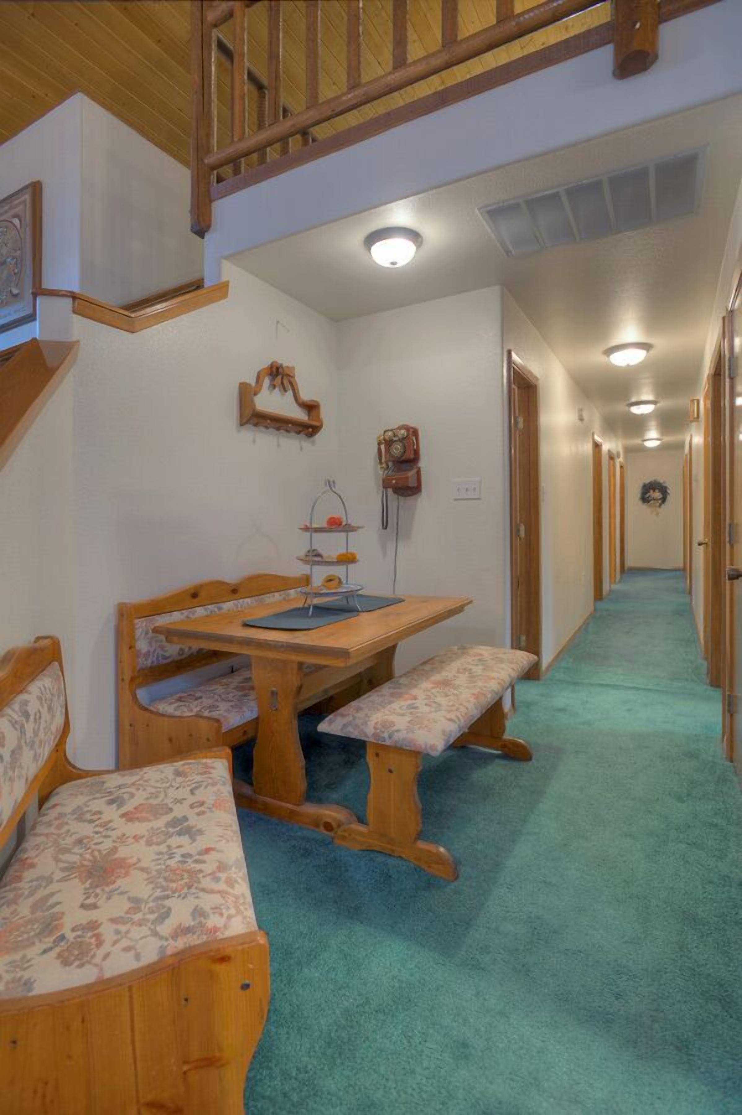 Un couloir avec un banc en bois, une table sur laquelle repose un coussin à motifs floraux, et un téléphone.