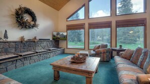 Una sala de estar acogedora con chimenea de piedra, ventanas amplias y un espacio de descanso confortable.