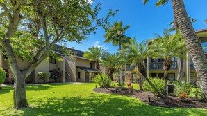 A courtyard with a lawn, palm trees, and a building with multiple balconies.