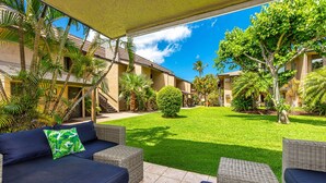 A covered outdoor area with wicker furniture and a well-maintained lawn.