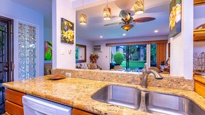 A kitchen with granite countertops, stainless steel sinks, and a dishwasher. There are hanging pendant lights and a ceiling fan.