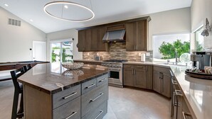 Una cucina moderna con mobili in legno scuro, un'isola centrale con cassetti, un forno integrato e un'ampia finestra che offre luce naturale.